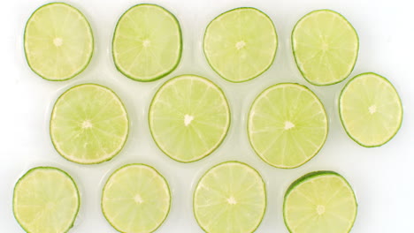 On-a-white-background-sliced-pieces-of-lime-are-sprinkled-with-water.-Juicy-fresh-lime-in-slow-motion.-Lots-of-lime-slices.
